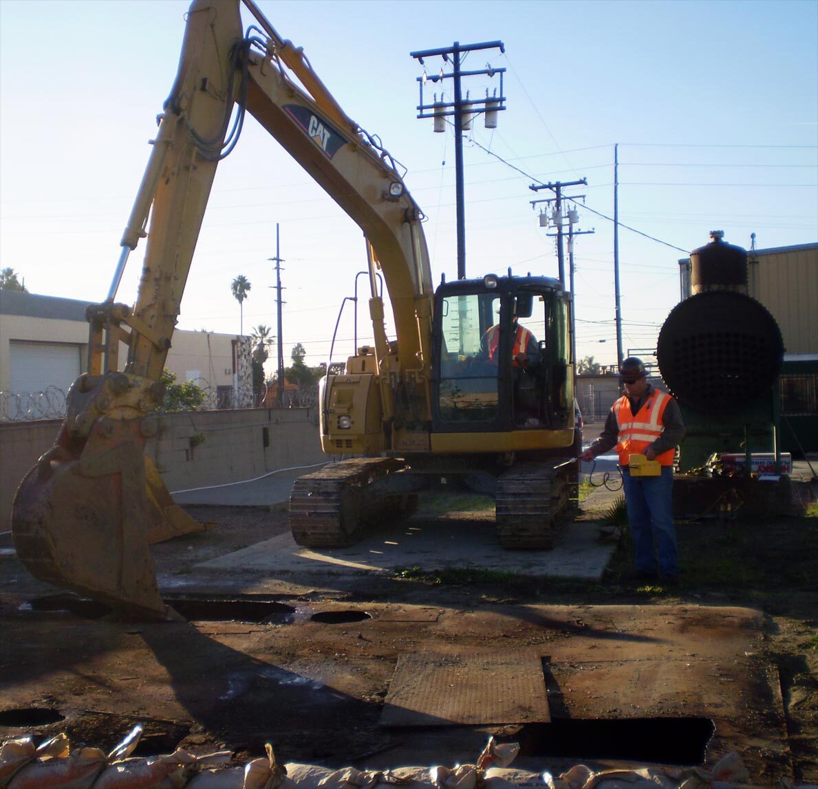 A tracked excavator and a field technician working over an open excavation at a petroleum release site.